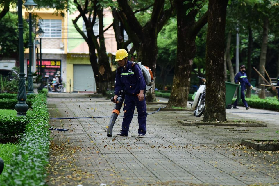 A city worker wearing protective gear uses a leaf blower to clean a public park pathway. A city worker wearing protective gear uses a leaf blower to clean a public park pathway.