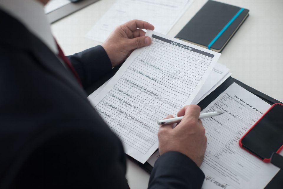 A businessman in a black suit reviews a printed application form with a pen on his desk. A businessman in a black suit reviews a printed application form with a pen on his desk.
