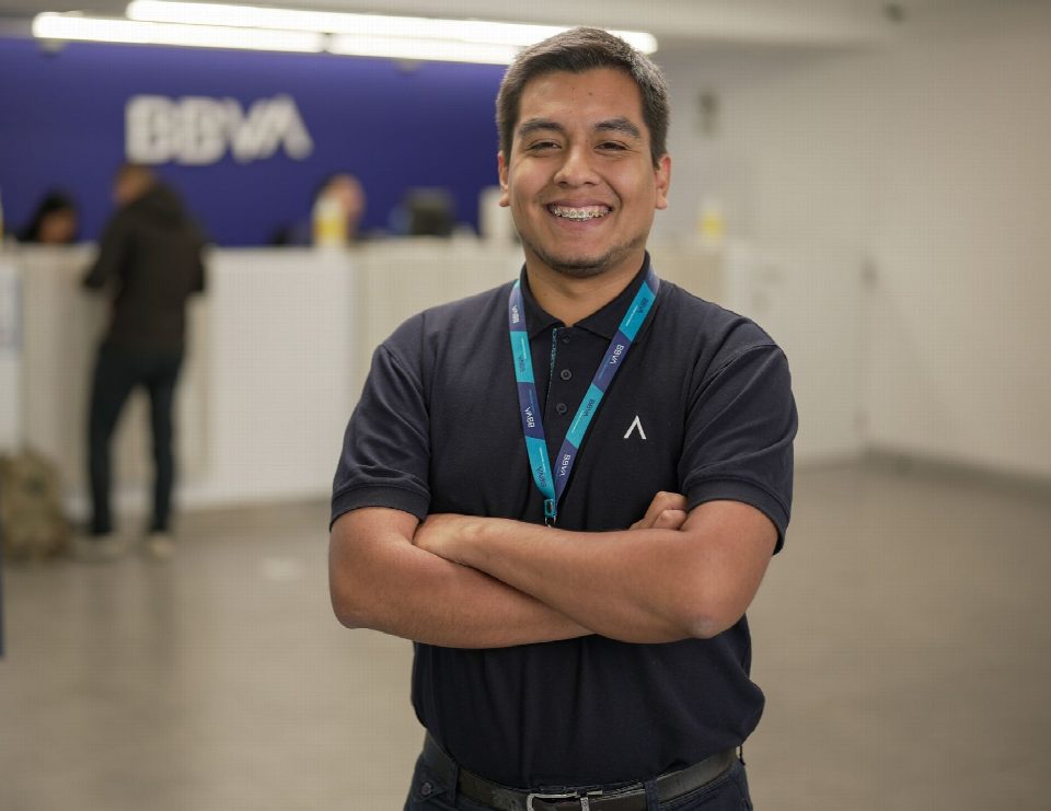 Confident bank employee standing with arms crossed at BBVA reception area, smiling warmly.