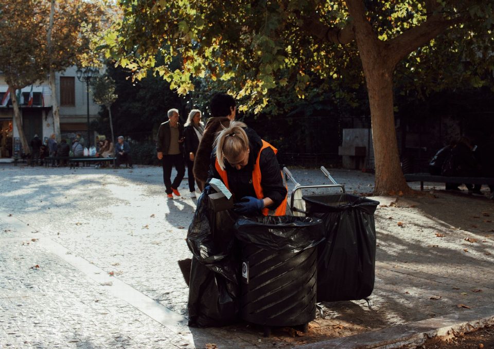 Sanitation worker in orange vest collecting trash in urban park during fall. Sanitation worker in orange vest collecting trash in urban park during fall.